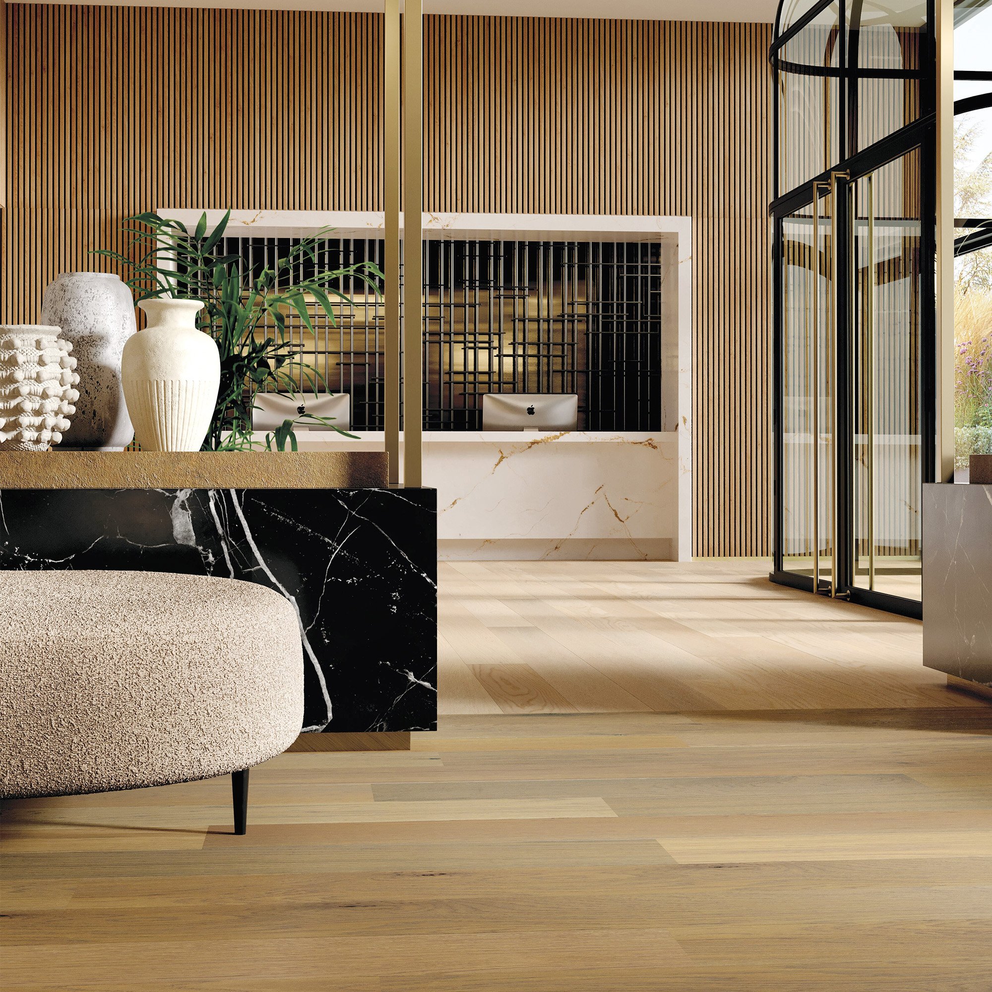 A interior image of a room with warm wood tones on showcasing functional performance of wood in floor and walls, placed against a black marble divider, neutral vases and a pouf opening up to large floor to ceiling glass windows. 