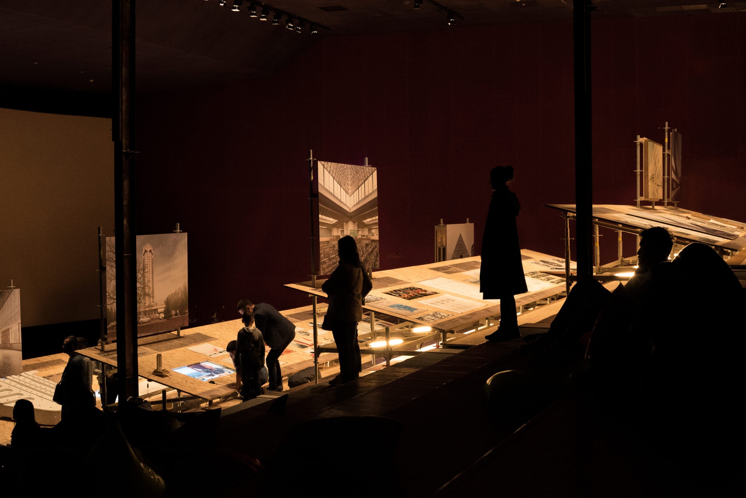 A back lit flooring with people interacting and reading about the art installations in a dark space. 