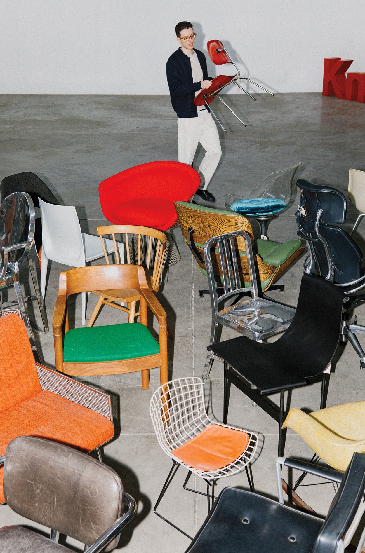 cofounder picking up a Eames chair and placing it in a pile of other vintage chairs together in the open concrete floor of the rarify warehouse. 