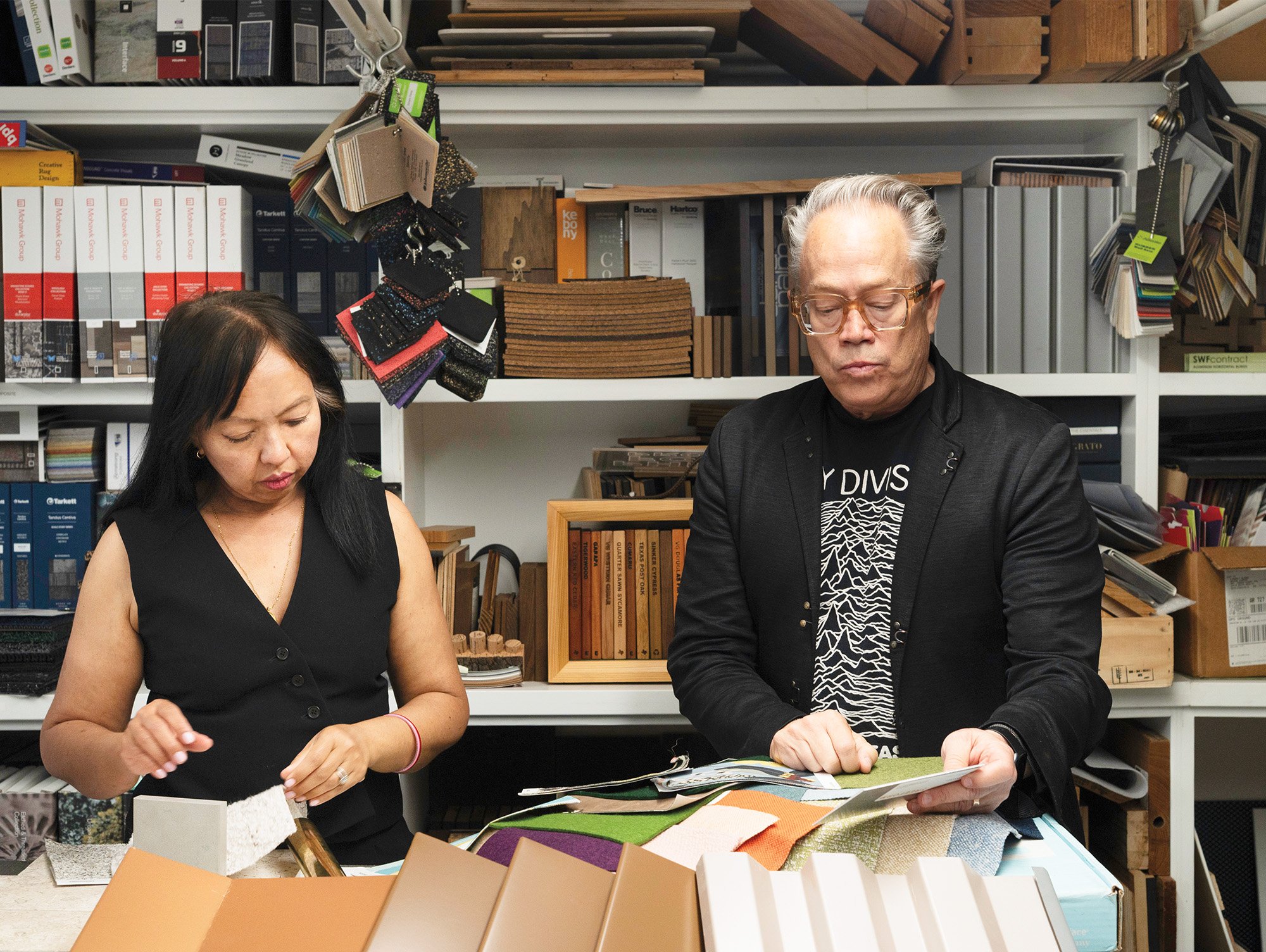 Marlon Blackwell and Ati Blackwell choosing material samples holding textile swatches and cladding, with a wall of materials behind them. 