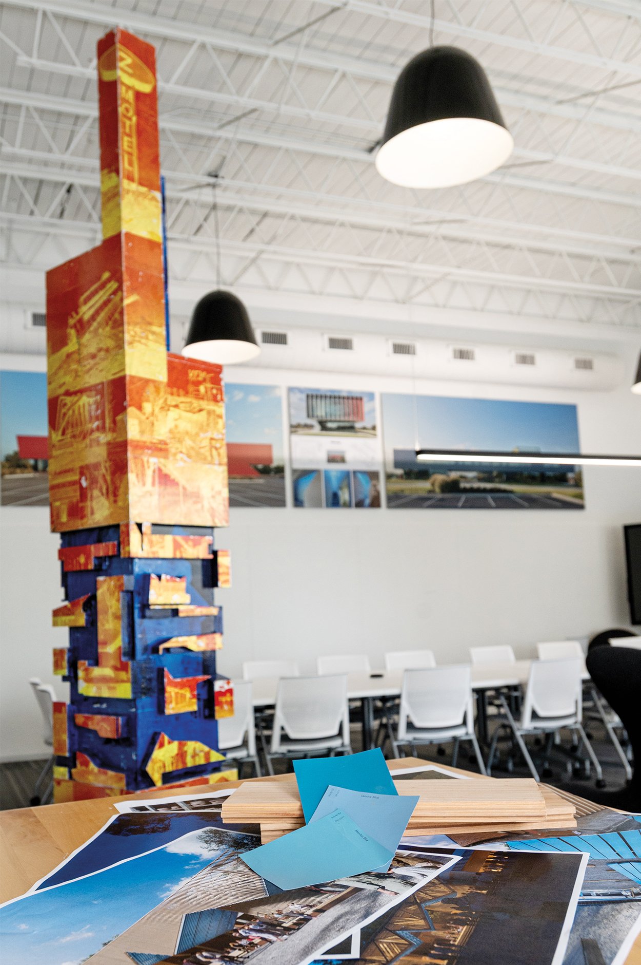 A 3D pillar covered with pieces and painted blue and orange and a table full of materials samples of wood and blue paint swatches with site images. 
