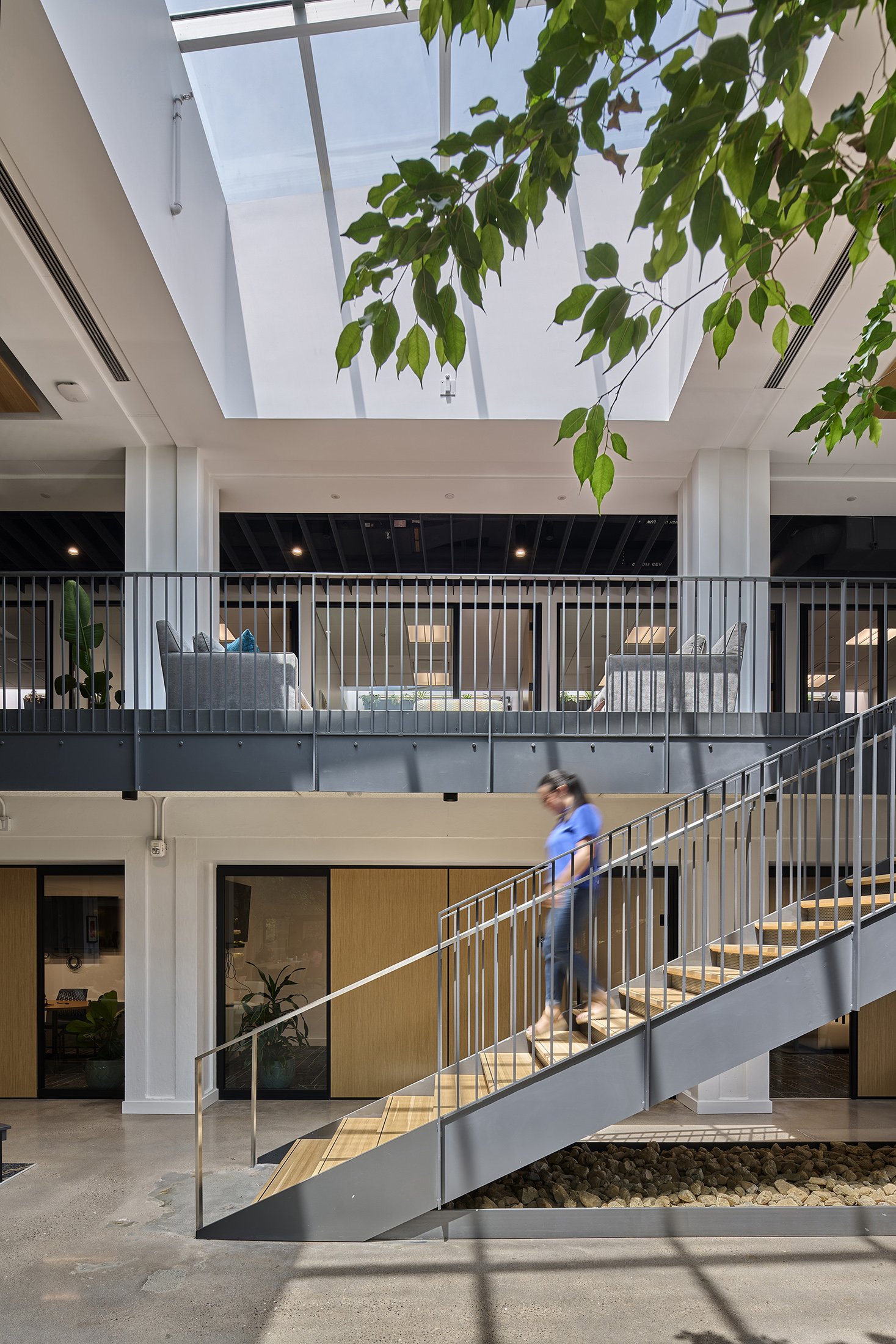 A person walking on metal and wooden staircase open to skylight. 