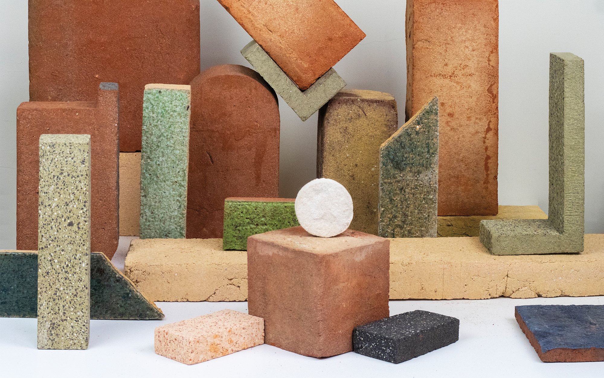 Multiple blocks with curved corners and edged corners in earthy colors made from waste materials and a white ball like structure.